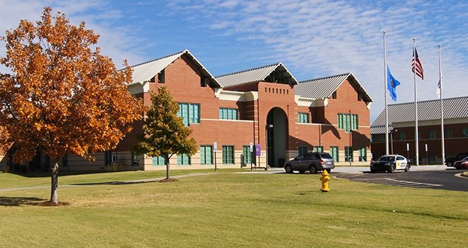 Entrance of 91Ӱ West Campus. Tree with orange leaves in the foreground. Oklahoma and American flags fly on flag poles.