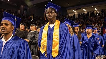Black male 91Ӱ graduate wears blue graduation cap and gown with gold Phi Theta Kappa Honors Society sash.